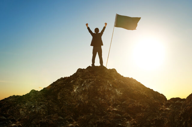 man on top of mountain achieving his goal