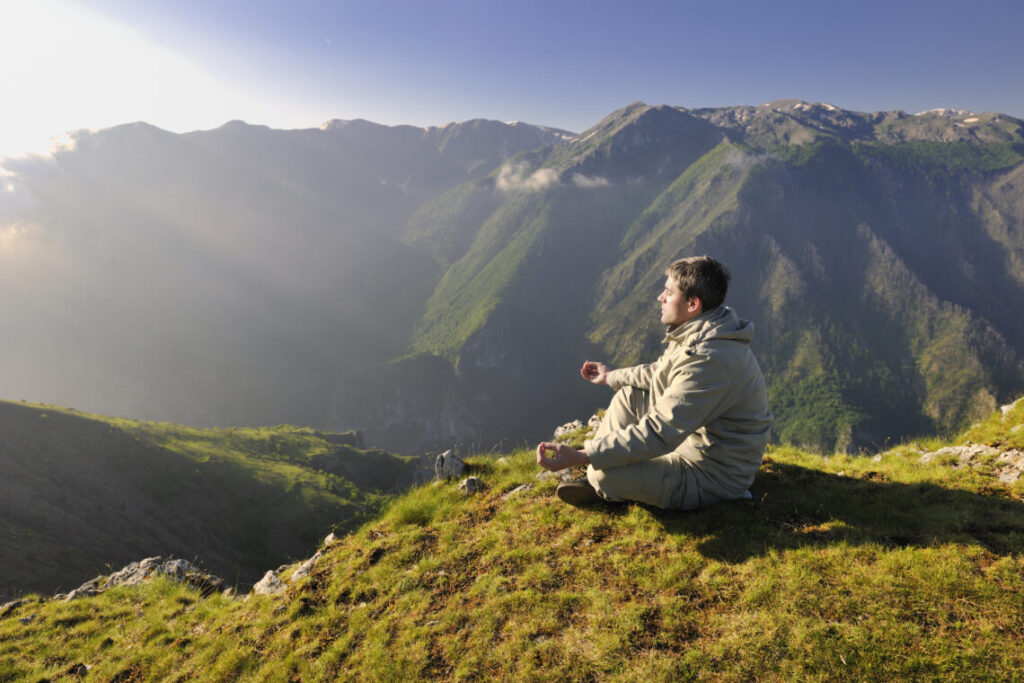 man taking some time out and meditating on the mountains during sunrise